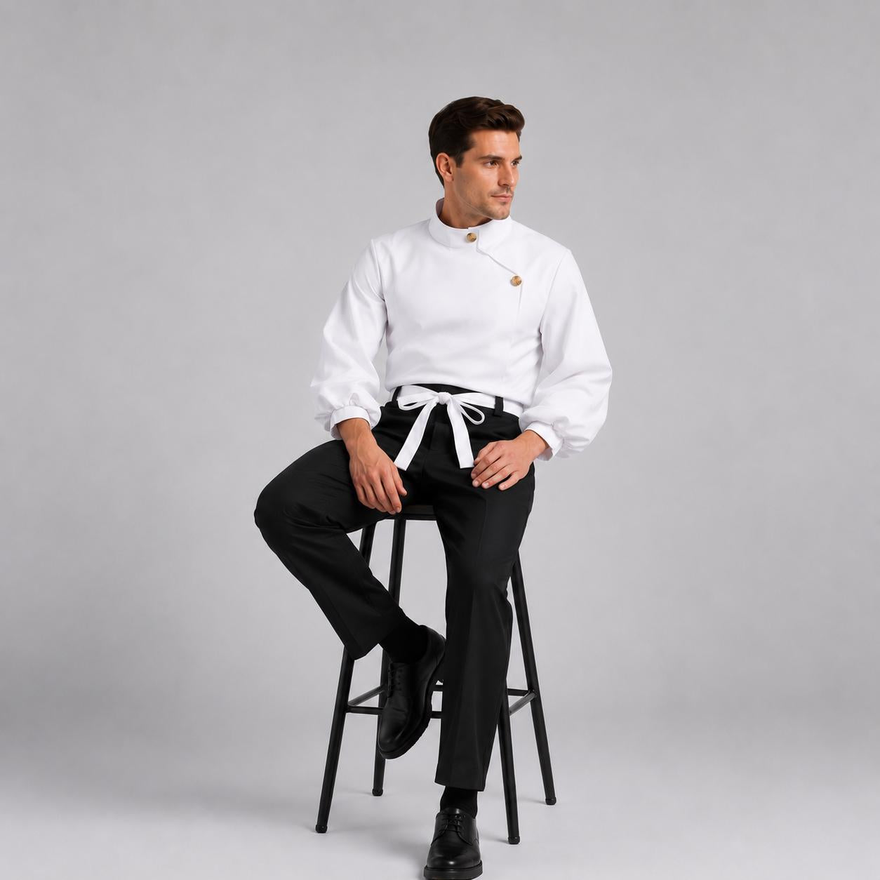 May include: A white long-sleeved shirt with a high collar, two visible buttons, and full sleeves paired with black trousers and a white waist tie. The shirt features a crossover front design and is worn with black shoes while seated on a stool.