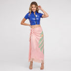 May include: A blue short-sleeved crop top with a front zipper and a white sun graphic, paired with a long, light pink wrap skirt featuring a green leaf pattern, a small orange flower detail, and a fringed hemline at the bottom edge.