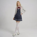 May include: A light gray blazer with pink lapel trim worn over a dark navy blue vest and a matching pleated skirt. The outfit includes a white collared shirt, a dark red bow tie, white over-the-knee socks, and white loafers with gold-tone hardware.