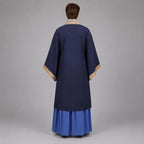 May include: A dark blue robe featuring wide sleeves with tan patterned trim along the collar and cuffs. The garment is worn over a bright blue pleated skirt that reaches the floor. The view shows the back of the attire with a solid color design.
