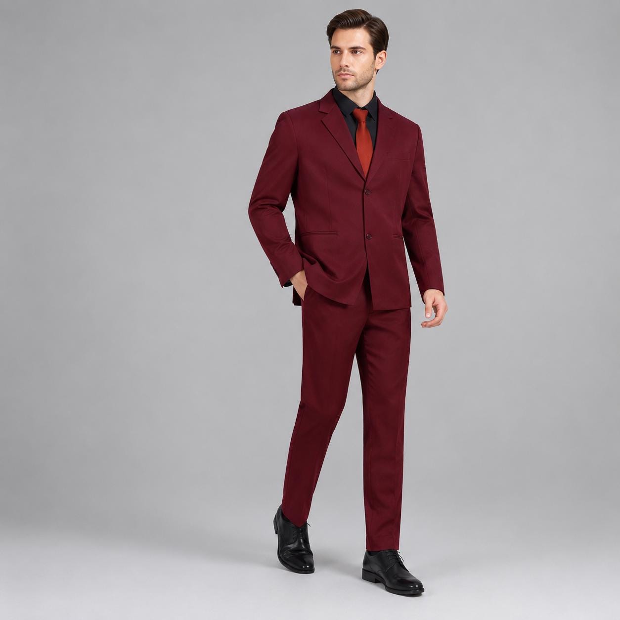 May include: A deep burgundy two-piece suit consisting of a single-breasted blazer with two buttons and matching trousers. The suit is worn over a black button-down shirt and a solid red necktie. The ensemble is completed with black leather shoes.