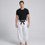 May include: A black short-sleeved crew neck t-shirt paired with loose-fitting white trousers. The trousers feature a high-waisted design with a black fabric belt tied in a bow at the center front and gathered elastic cuffs at the ankles.