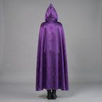 May include: A long, hooded cape in a vibrant purple hue. The cape is made of a soft, flowing fabric, and the hood is pointed. The person is wearing black boots. The cape drapes down to the ankles, creating a dramatic silhouette.